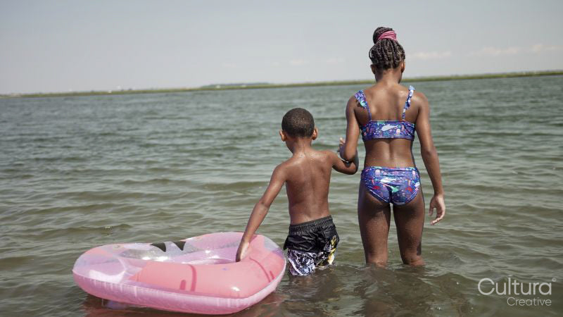 Rear view of brother and sister wading in sea with inflatable ring