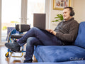 Man with headphones using laptop on sofa, wheelchair in background