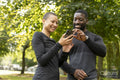 Smiling athletic man and woman looking at smart phone in park