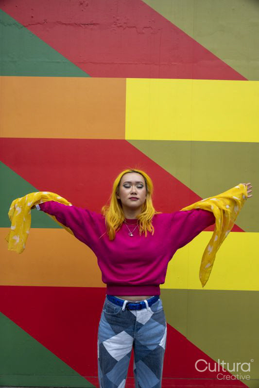 Young woman with yellow hair standing against colorful wall