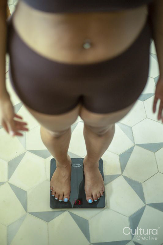 Low section of woman in lingerie standing on bathroom scale