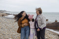 Grandmother, mother and daughter laughing while walking on beach on cloudy day