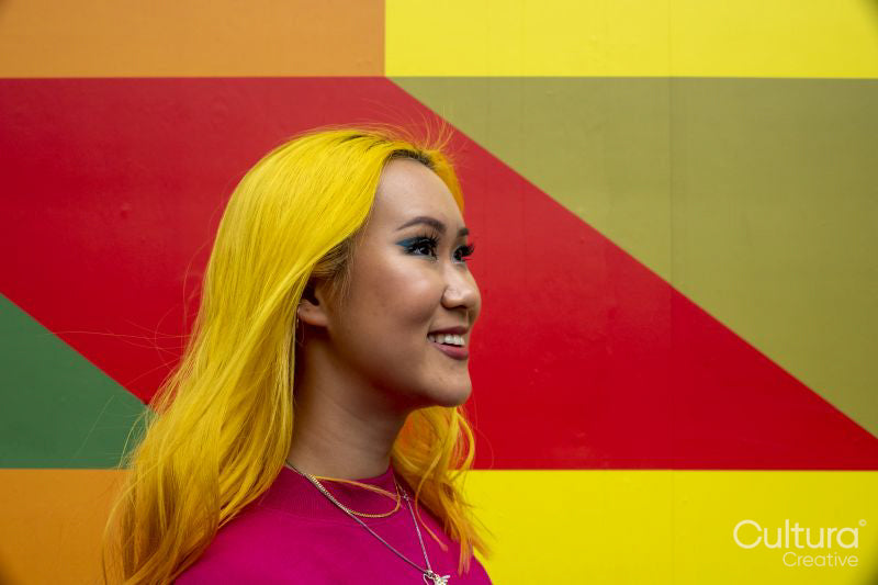 Smiling young woman with yellow hair against colorful wall