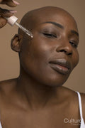 Studio portrait of woman with shaved head applying oil on face