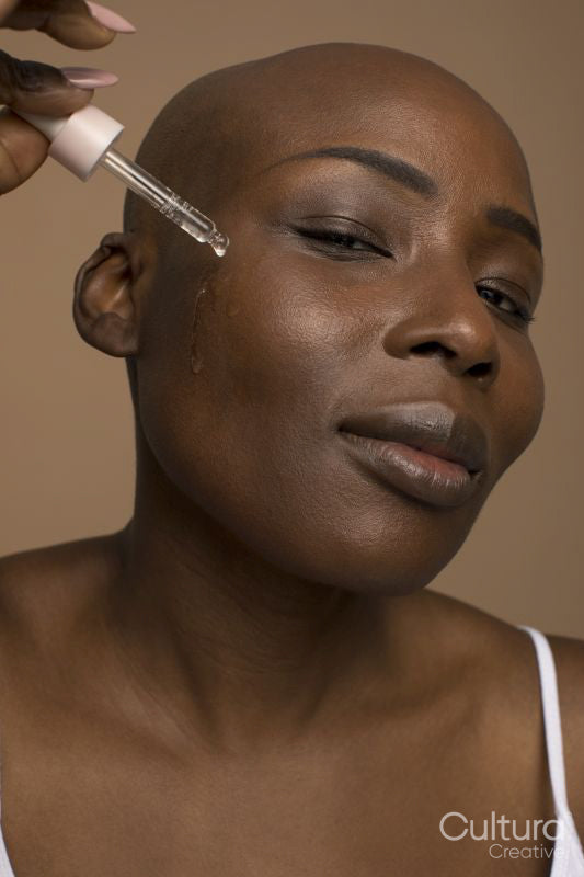 Studio portrait of woman with shaved head applying oil on face
