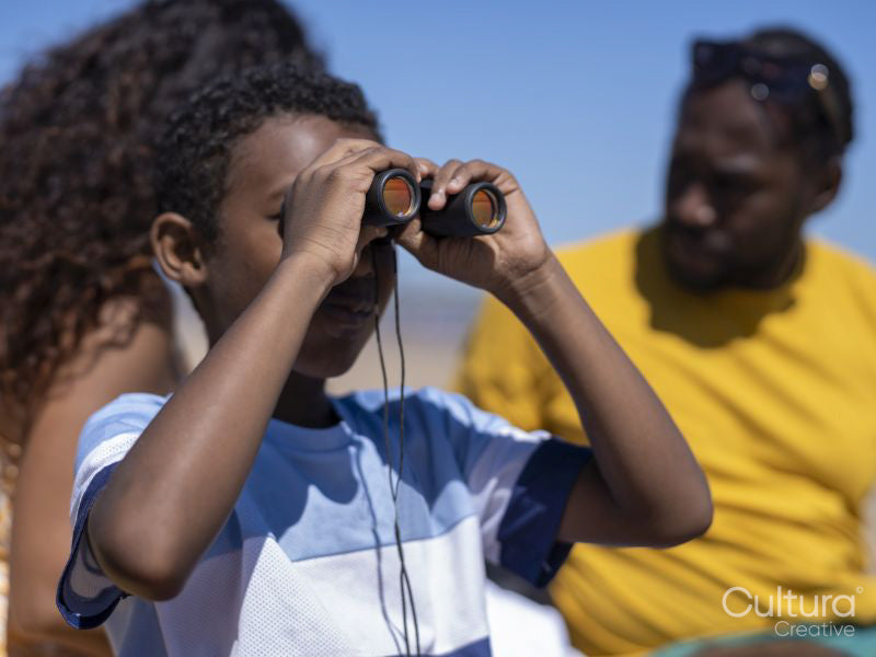 Boy looking through binoculars on beach