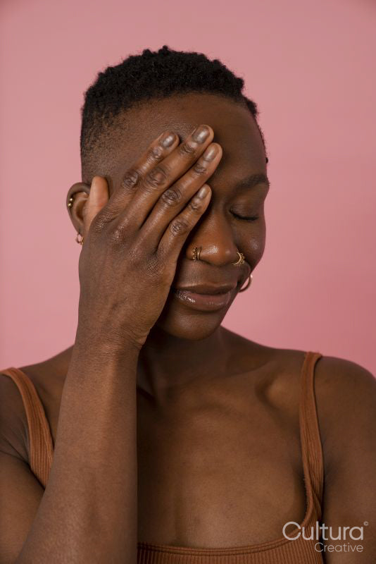 Smiling young woman covering face against pink background