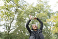 Portrait of smiling woman with headphones raising arms in park