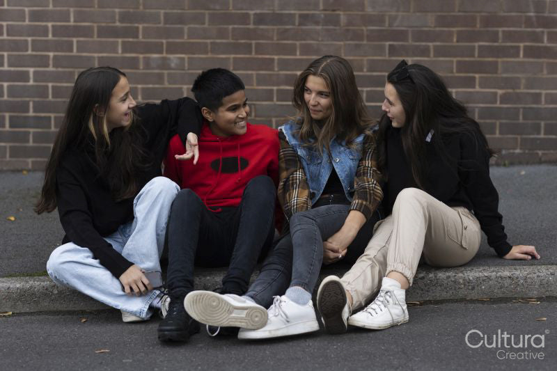 Smiling friends talking while sitting on curb