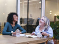 Two smiling women writing in notebooks in modern office