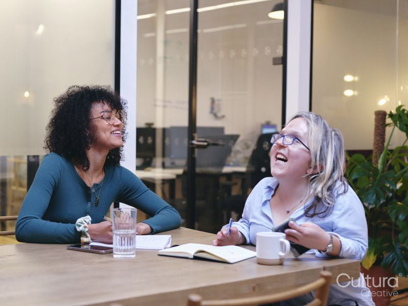 Two smiling women writing in notebooks in modern office