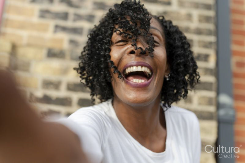 Portrait of woman laughing while taking selfie against brick wall