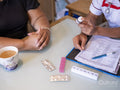 Nurse and mature woman sitting at table, holding medications
