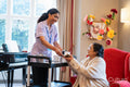 Female employee serving tea to senior woman in nursing home