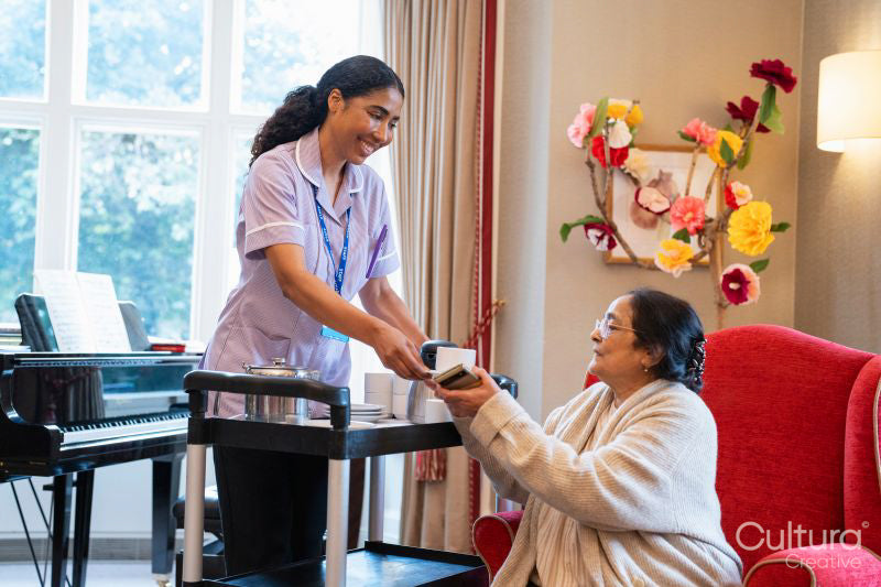 Female employee serving tea to senior woman in nursing home