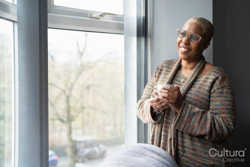 Mature woman with coffee cup looking through window