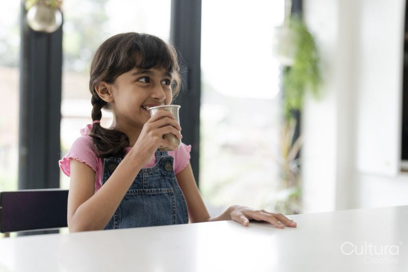 Little girl drinking from mug at table