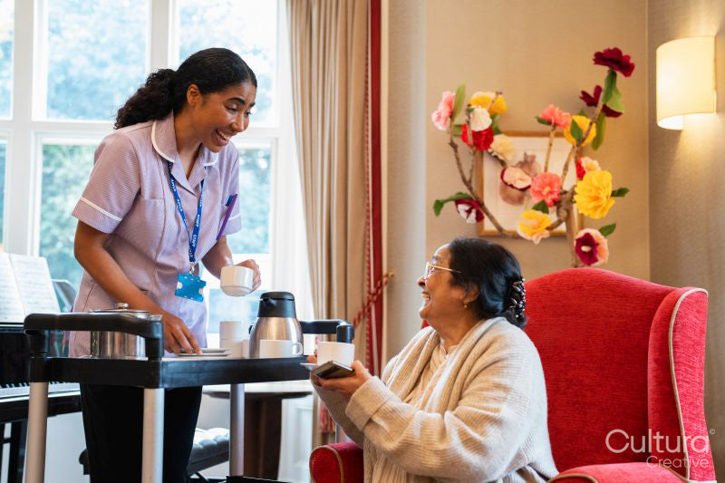 Female employee serving tea to senior woman in nursing home