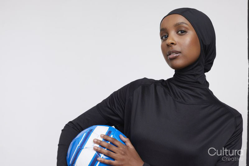 Studio portrait of young woman in hijab holding soccer ball