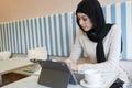 Young woman in hijab using tablet in cafe