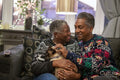 Senior couple wearing Christmas sweaters sitting on sofa with cat