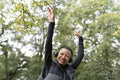 Portrait of smiling woman with headphones raising arms in park