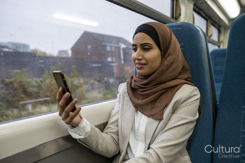 Smiling woman in hijab looking at mart phone in commuter train