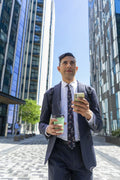 Businessman walking in business district with coffee and using phone