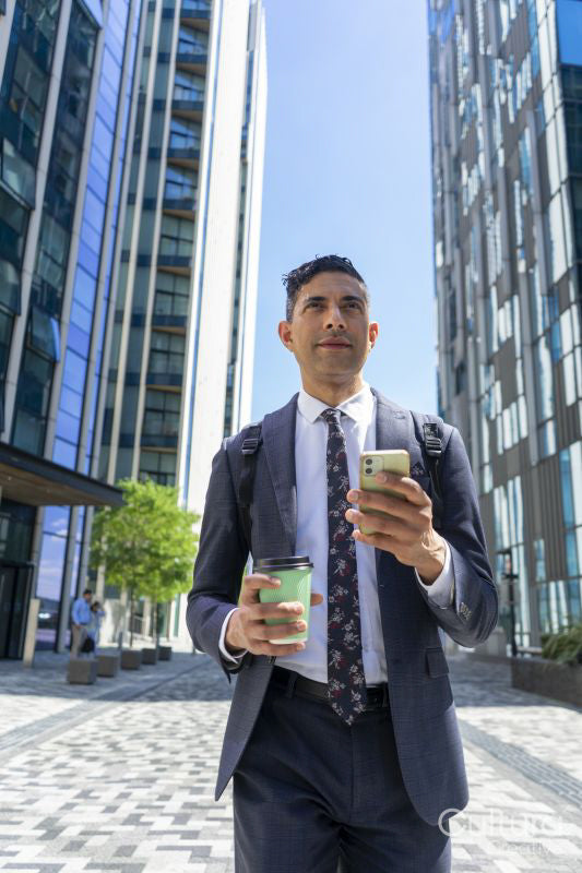 Businessman walking in business district with coffee and using phone