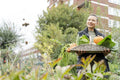 Portrait of smiling woman holding basket with fresh vegetables in urban garden