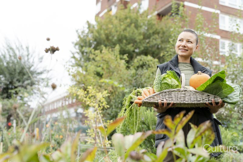 Portrait of smiling woman holding basket with fresh vegetables in urban garden