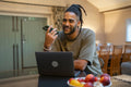 Man with dreads talking on phone and working on laptop at home