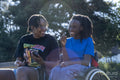 Teenage girl in wheelchair with friend relaxing in park