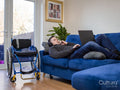 Man with headphones and laptop lying on sofa next to wheelchair