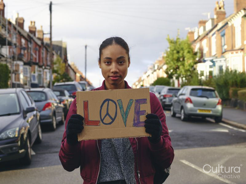 Woman on street holding protest sign with symbol of peace