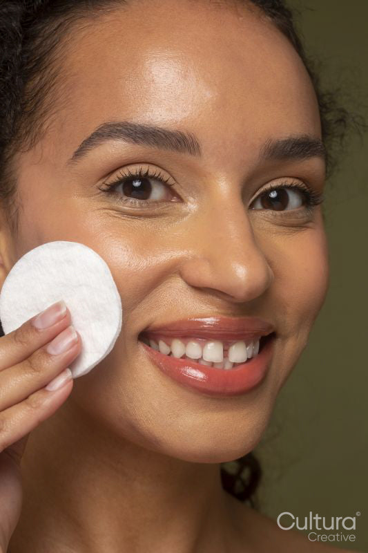Close-up of smiling woman rubbing cheek with cotton pad