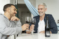 Male couple raising toast with red wine at home