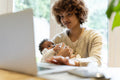 Mother holding baby daughter and using laptop at home