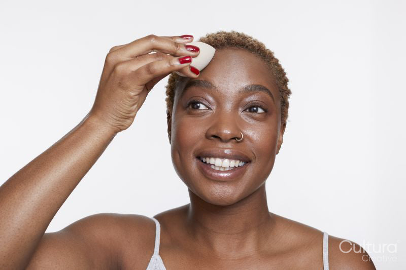 Studio portrait of smiling woman applying make up foundation with sponge