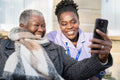 Smiling nurse and senior woman looking at phone outdoors