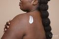 Studio shot of young woman applying moisturizer on back