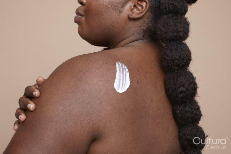 Studio shot of young woman applying moisturizer on back