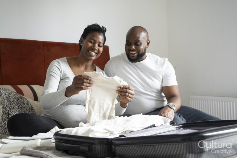 Pregnant woman and man holding baby clothing on bed