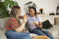Two young women sitting on sofa and eating pizza
