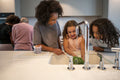 Smiling woman assisting daughter washing broccoli in kitchen sink