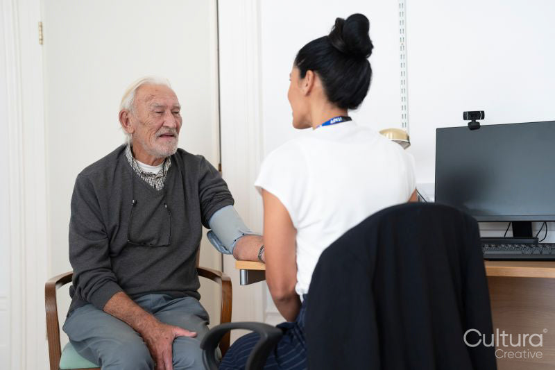 Female doctor taking senior patients blood pressure in office