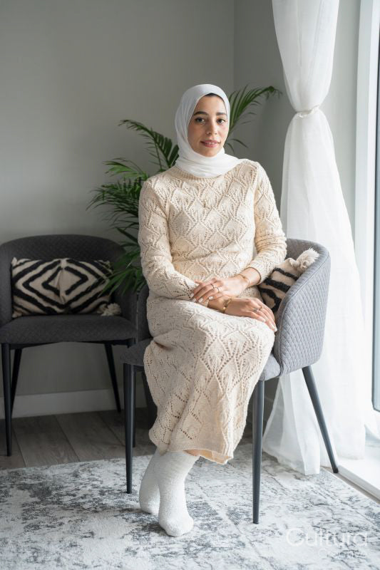 Portrait of smiling woman in hijab sitting in chair at home