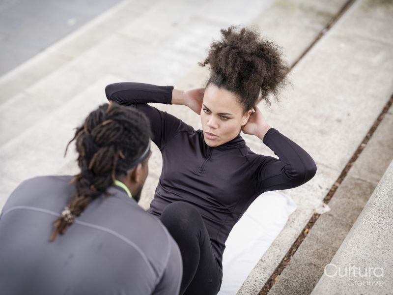 Man assisting woman doing sit-ups outdoors