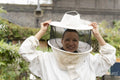 Portrait of smiling female beekeeper putting on protective hat in urban garden