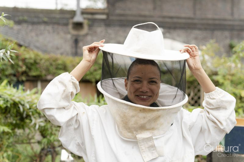 Portrait of smiling female beekeeper putting on protective hat in urban garden